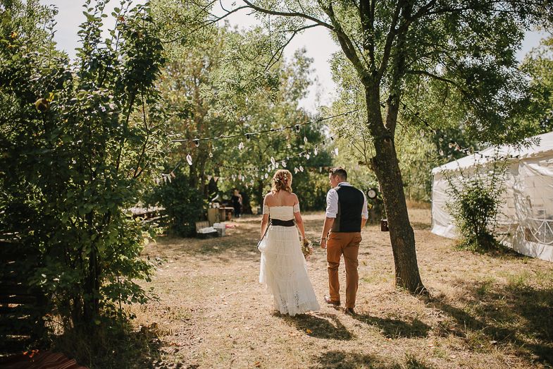 Newlywed couple walking hand in hand down a sunny forest path.