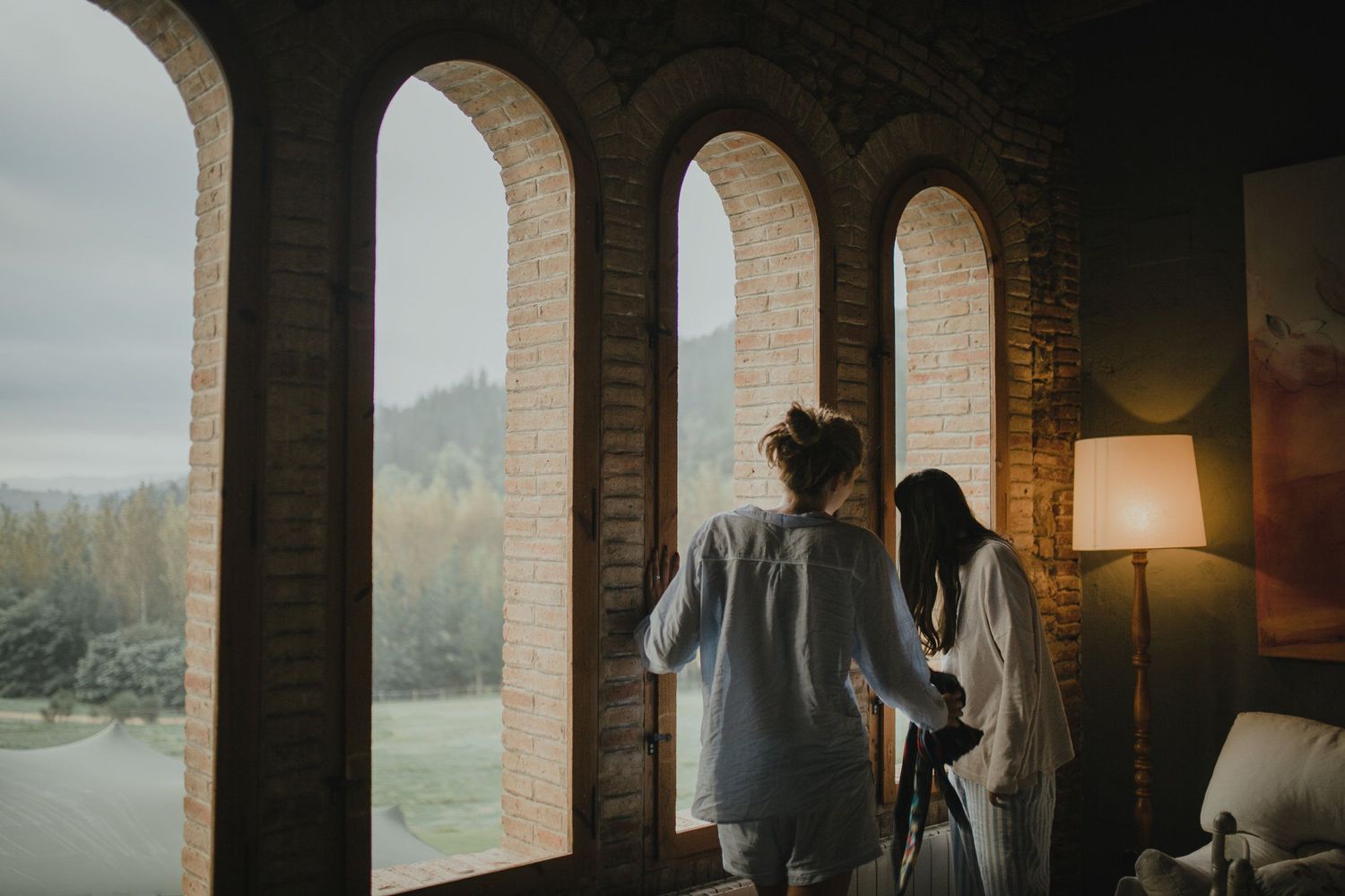 Silhouettes stand by arched windows overlooking mountain landscape at dusk.