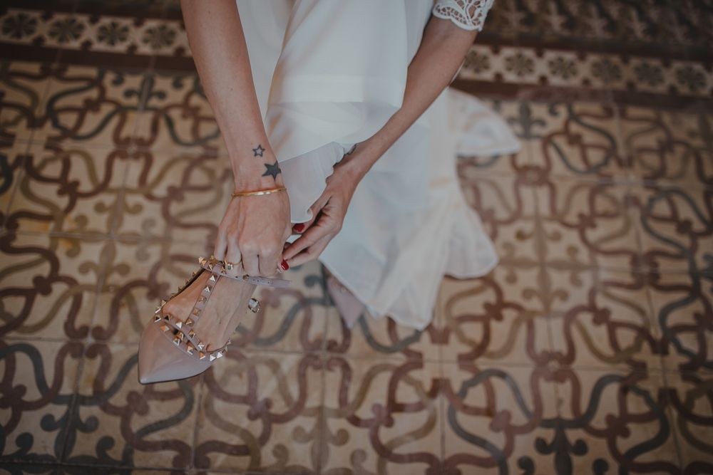 Close-up of hands holding elegant beige wedding shoes on a patterned floor.