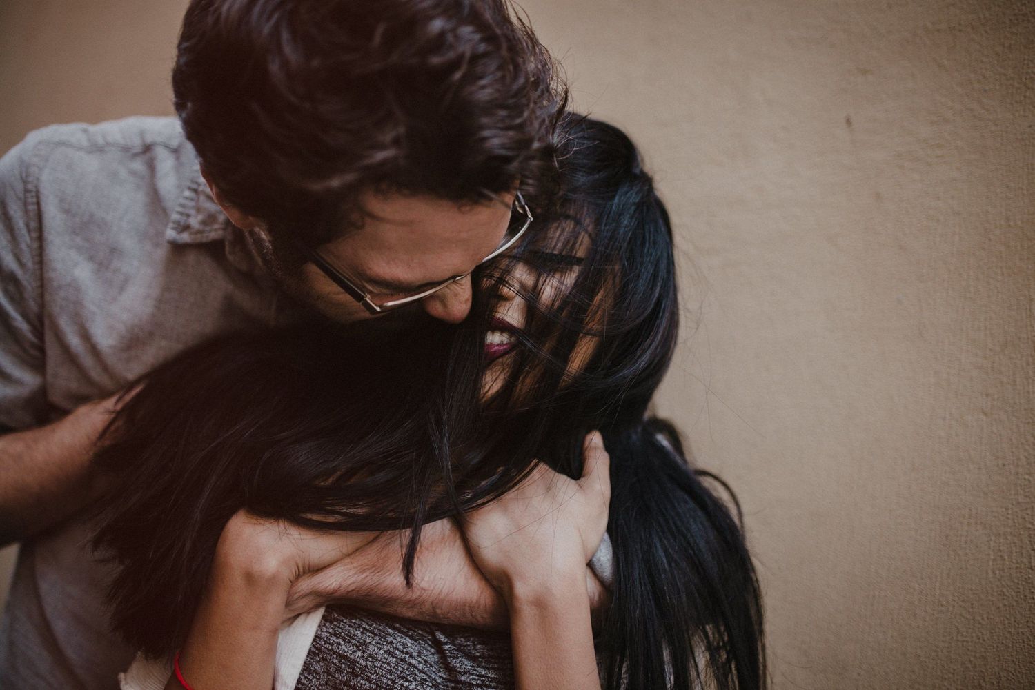 Emotional intimate moment captured in moody lighting against neutral wall background.