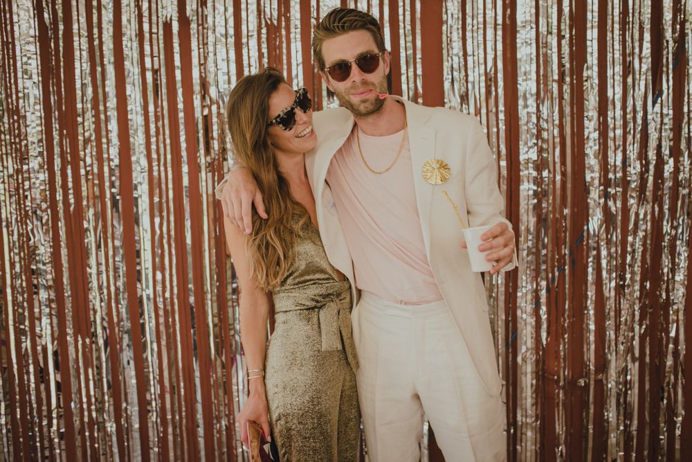 Stylish couple posing against a metallic fringe backdrop at an event.