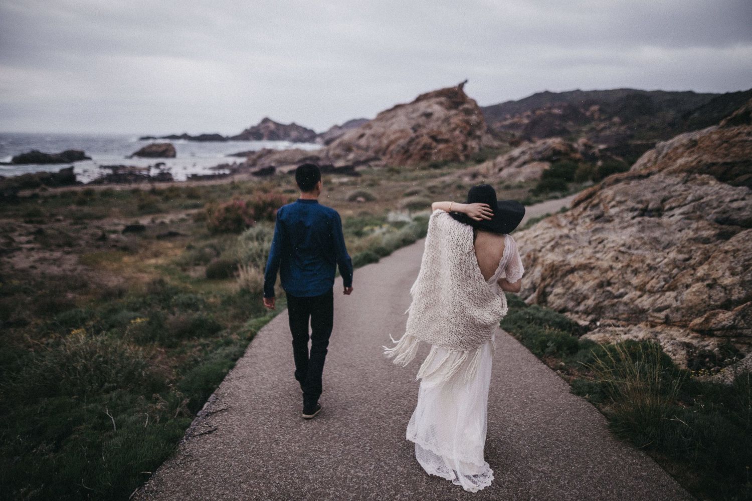 Couple walking down a coastal path surrounded by rugged seaside cliffs.