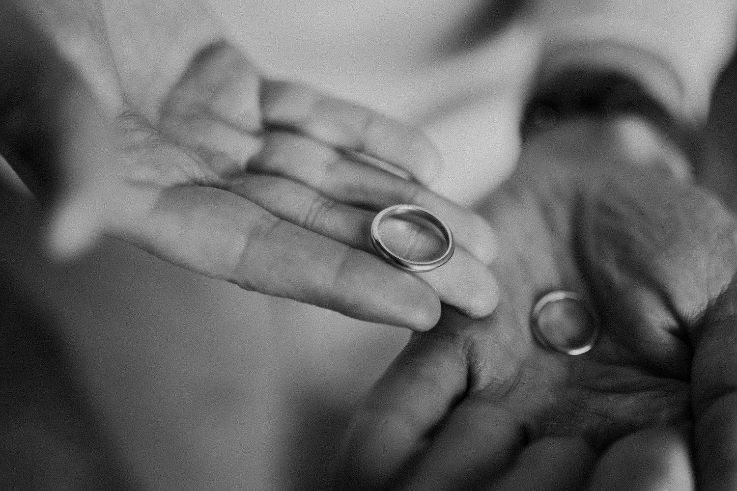 Wedding rings displayed on open palm in black and white photography.