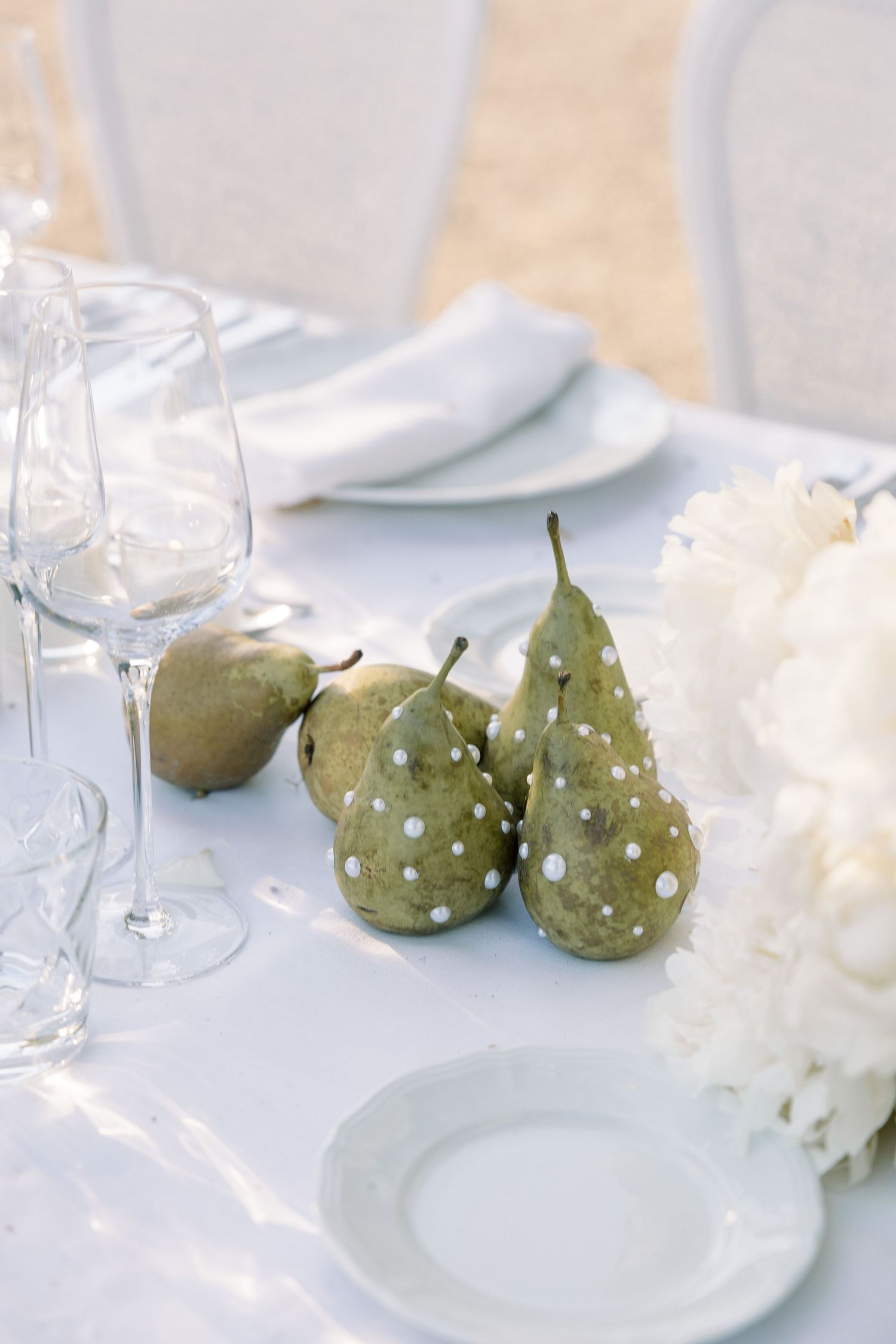 Elegant table setting with decorative pears and wine glasses on white tablecloth.