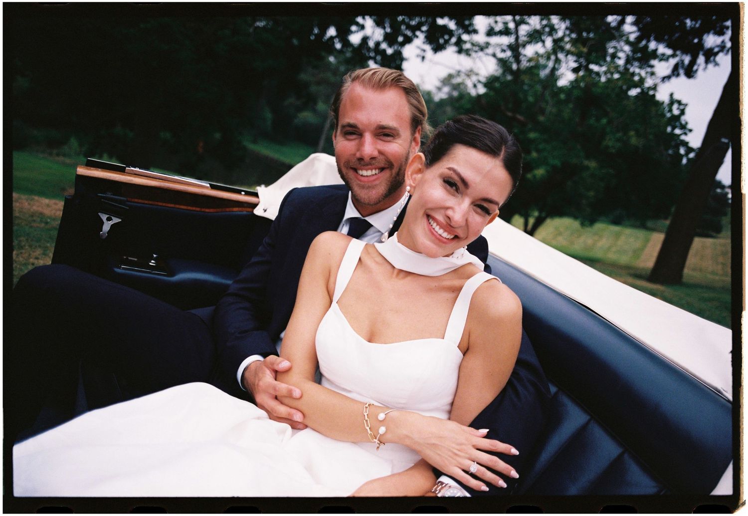 A happy couple smiles and embraces while sitting in a convertible car on a sunny day.