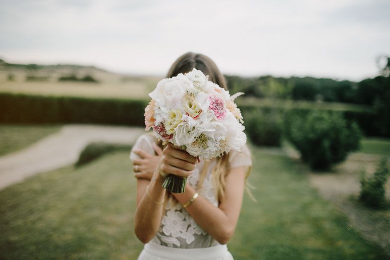 A wedding bouquet of white and pink peonies held up against a scenic countryside background.