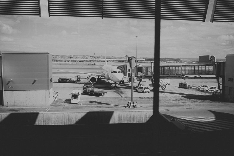 Black and white airport terminal view with planes visible through large windows.
