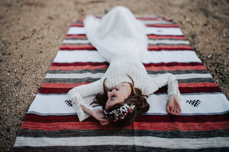 Bride laying on striped blanket in white dress against desert backdrop.