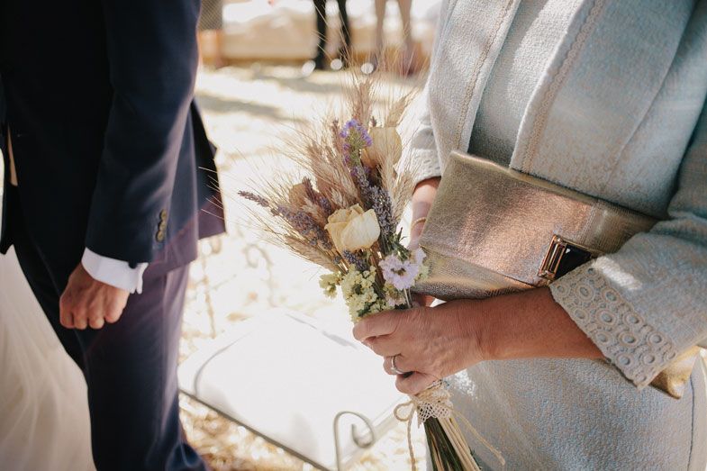 Close-up of delicate dried flower wedding bouquet held against a light-colored dress.