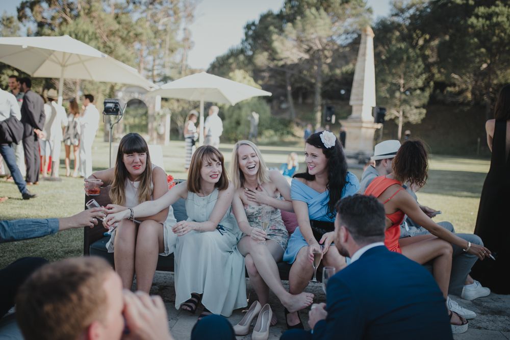 Wedding guests relaxing on grass during outdoor reception under blue sky.
