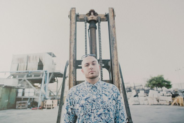 A person in a patterned blue shirt stands alone against industrial equipment.