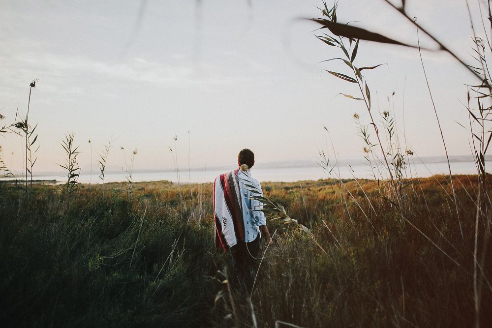 Person walking through tall grass at sunset in a serene landscape.