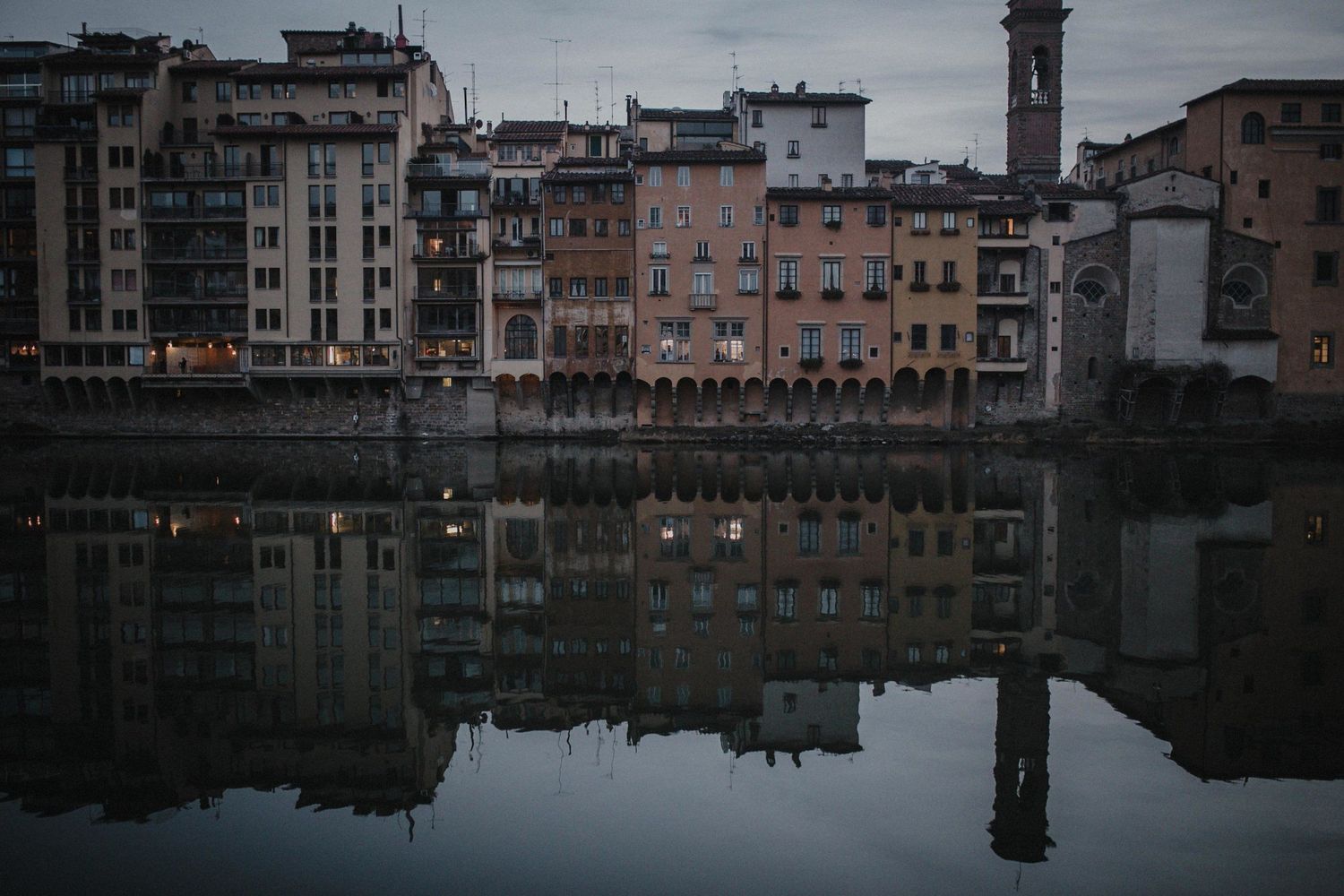 Historic buildings along the Arno River in Florence reflect perfectly in the calm water at dusk.