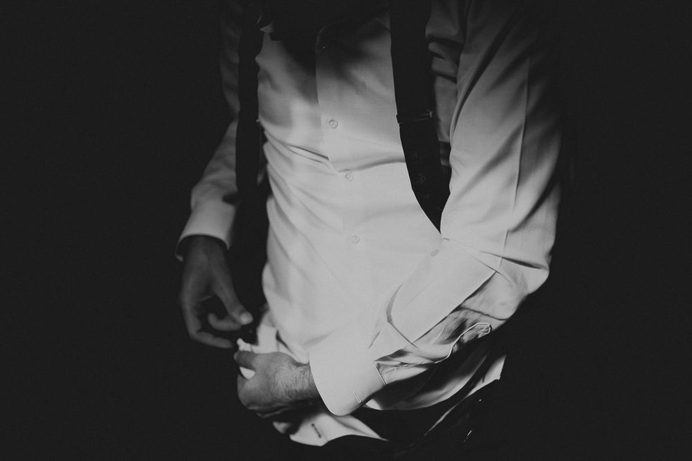 Close-up of hands adjusting white formal attire in dramatic lighting.