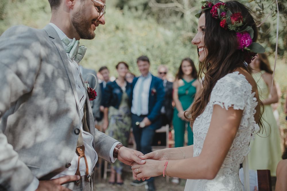 Garden wedding ceremony with couple exchanging rings as guests watch in the background.