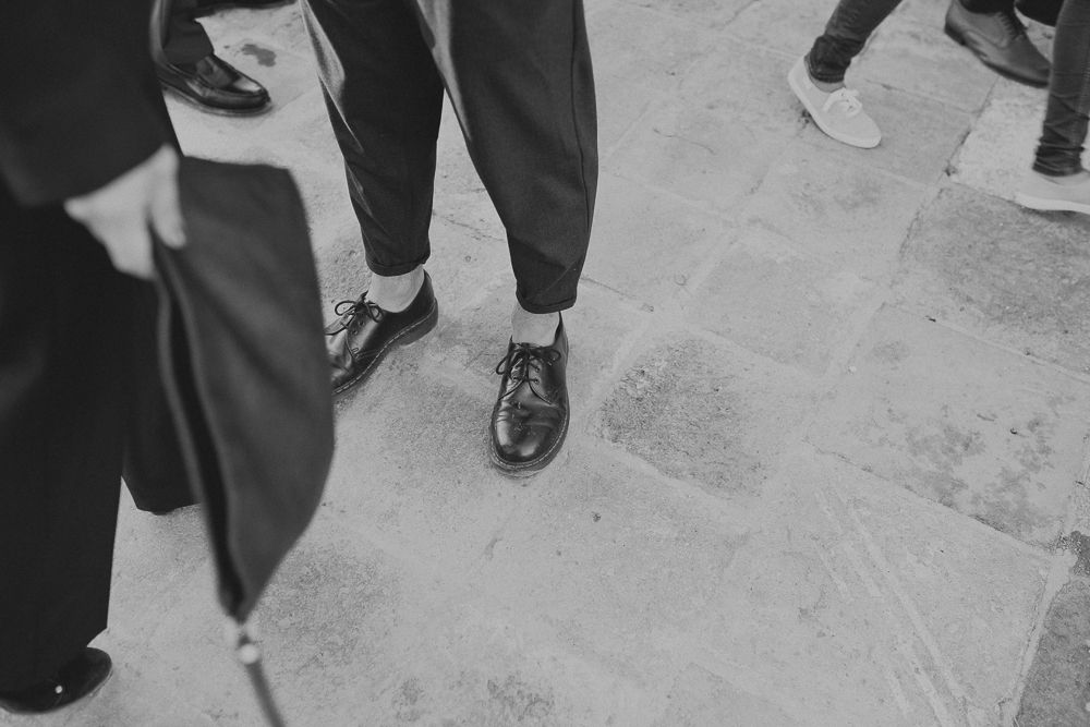 Close-up black and white shot of formal dress shoes and pants on a stone floor.