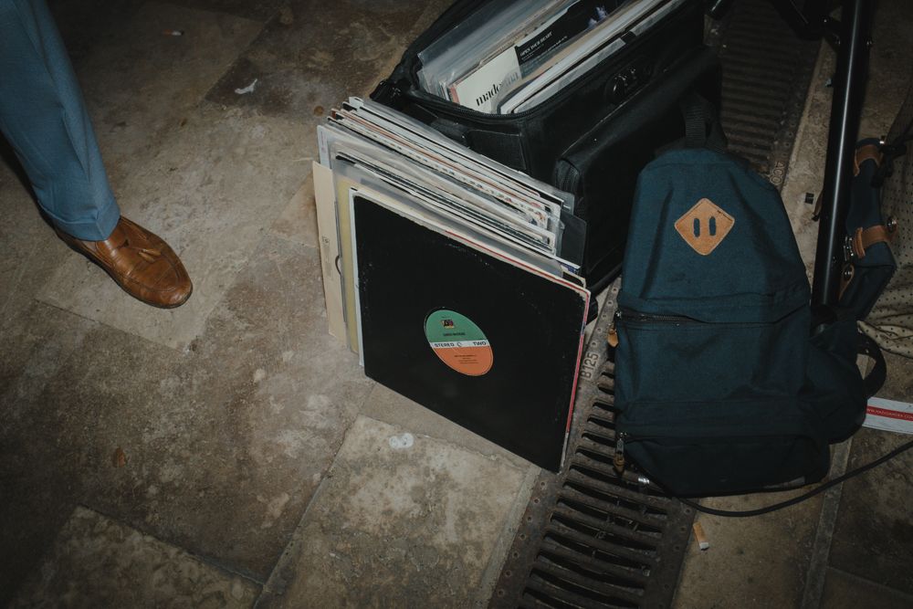 A navy blue backpack sits next to a stack of vinyl records on concrete floor.