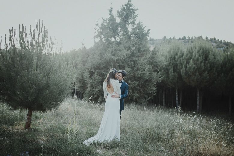 Ethereal wedding photo of a couple standing in a misty field surrounded by pine trees.