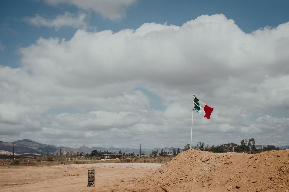 Red flag waves against cloudy sky over desert landscape with mountains in distance.