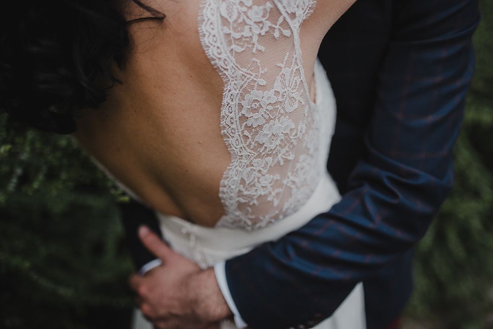 Close-up detail of a white lace wedding dress back and navy suit jacket.