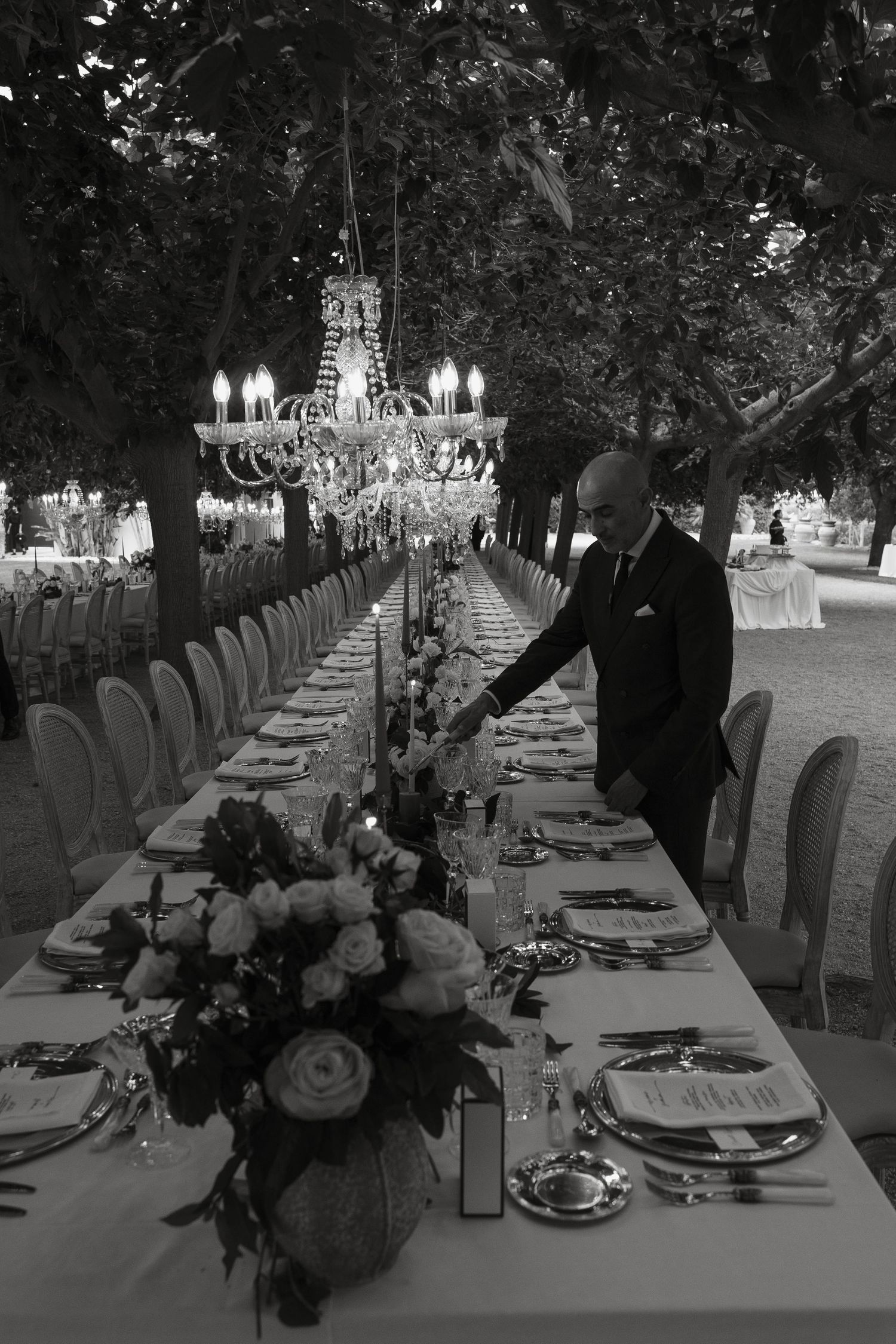 An elegant table setting under crystal chandeliers with white floral centerpieces.