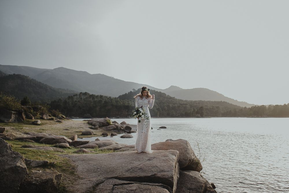 Figure in white dress stands on rocky outcrop overlooking misty mountain lake.