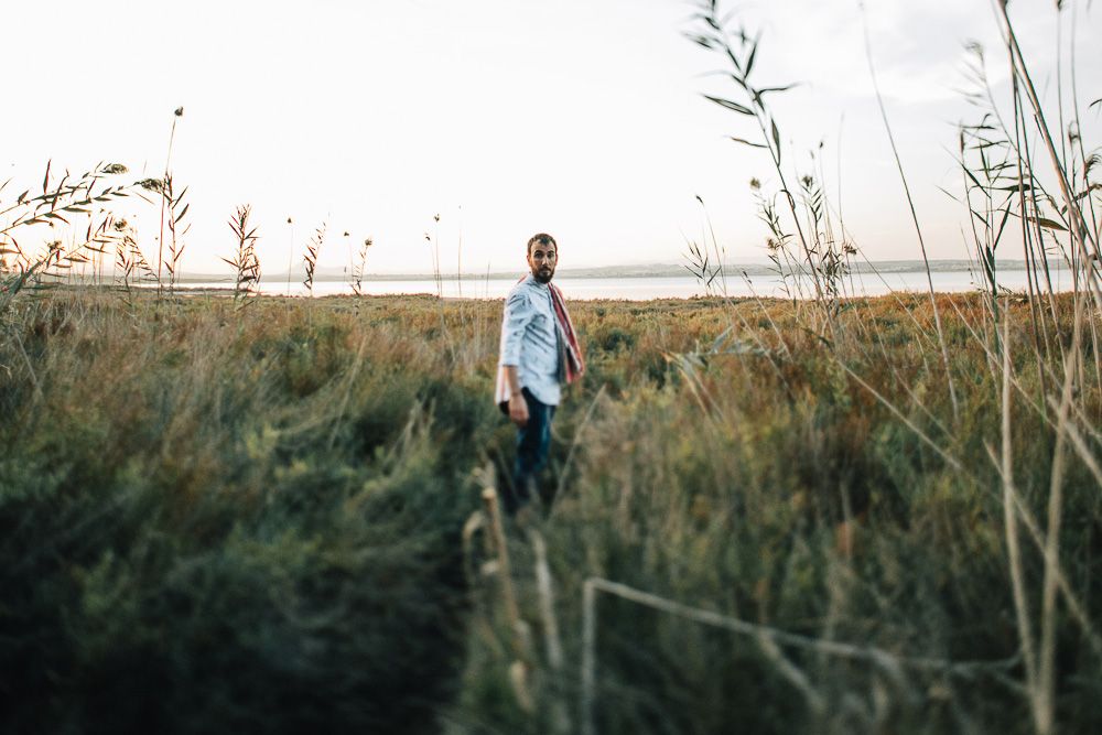 A person in a blue shirt stands alone in tall grass at sunset.
