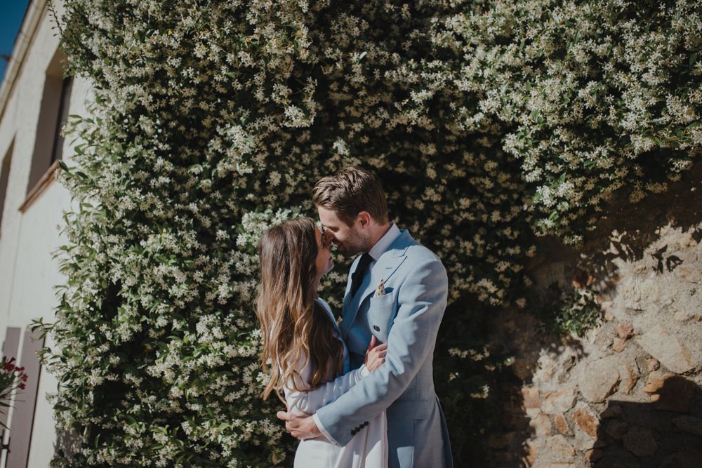 Intimate wedding moment against a wall of white flowering vines on a sunny day.