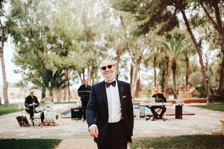 A formal gathering in an outdoor garden setting with musicians performing in the background.