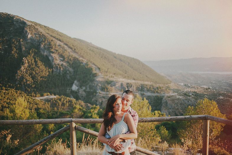 A couple shares an intimate moment overlooking a scenic mountain valley at sunset.