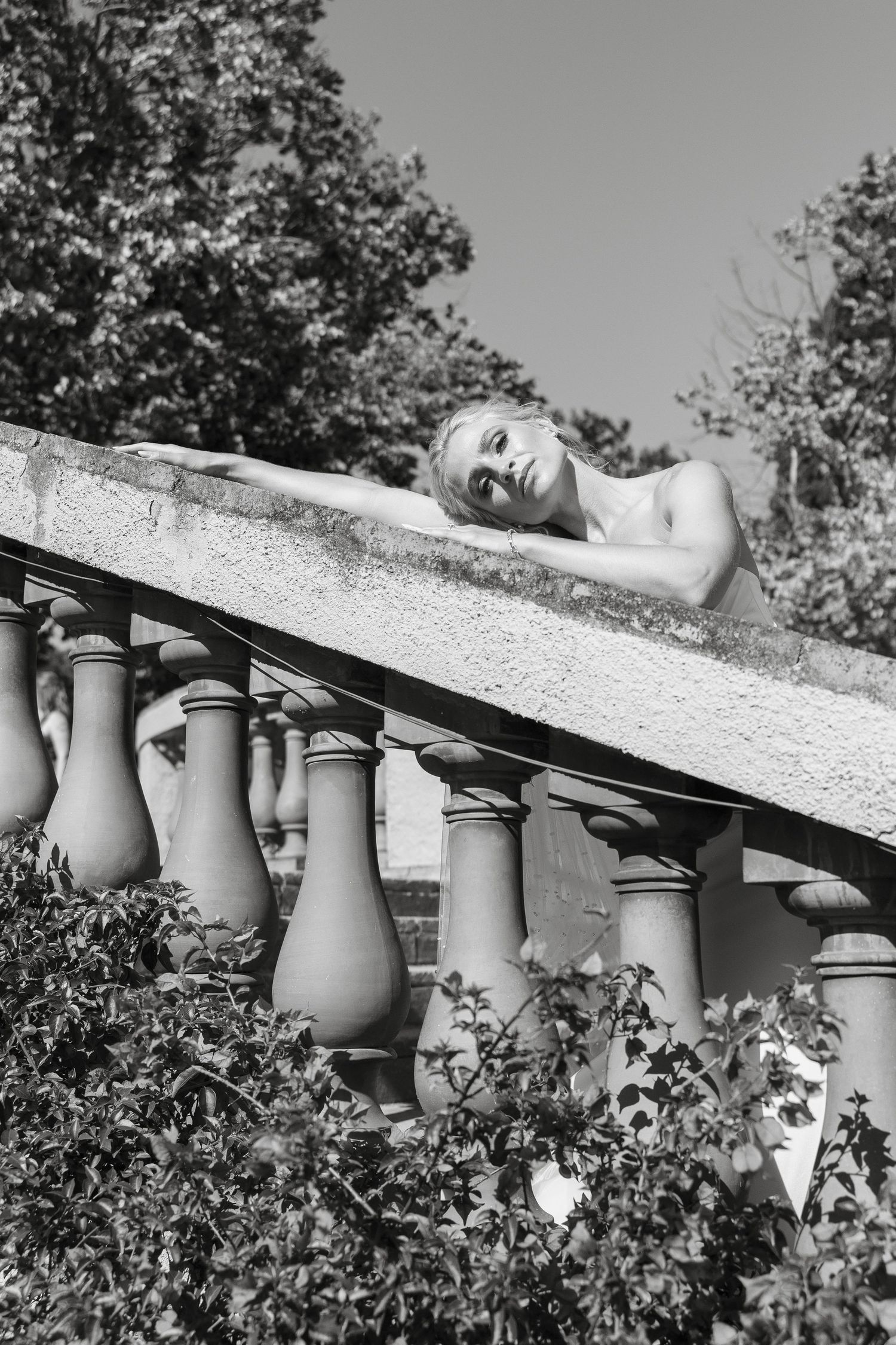Artistic black and white portrait of bride resting on stone balustrade.