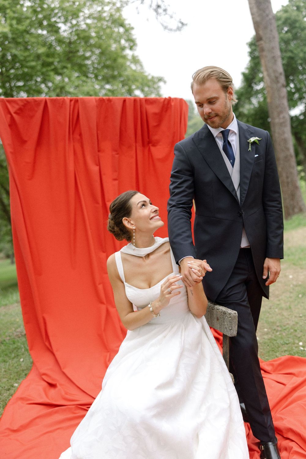 Wedding photo session against vibrant red backdrop in an outdoor garden setting.