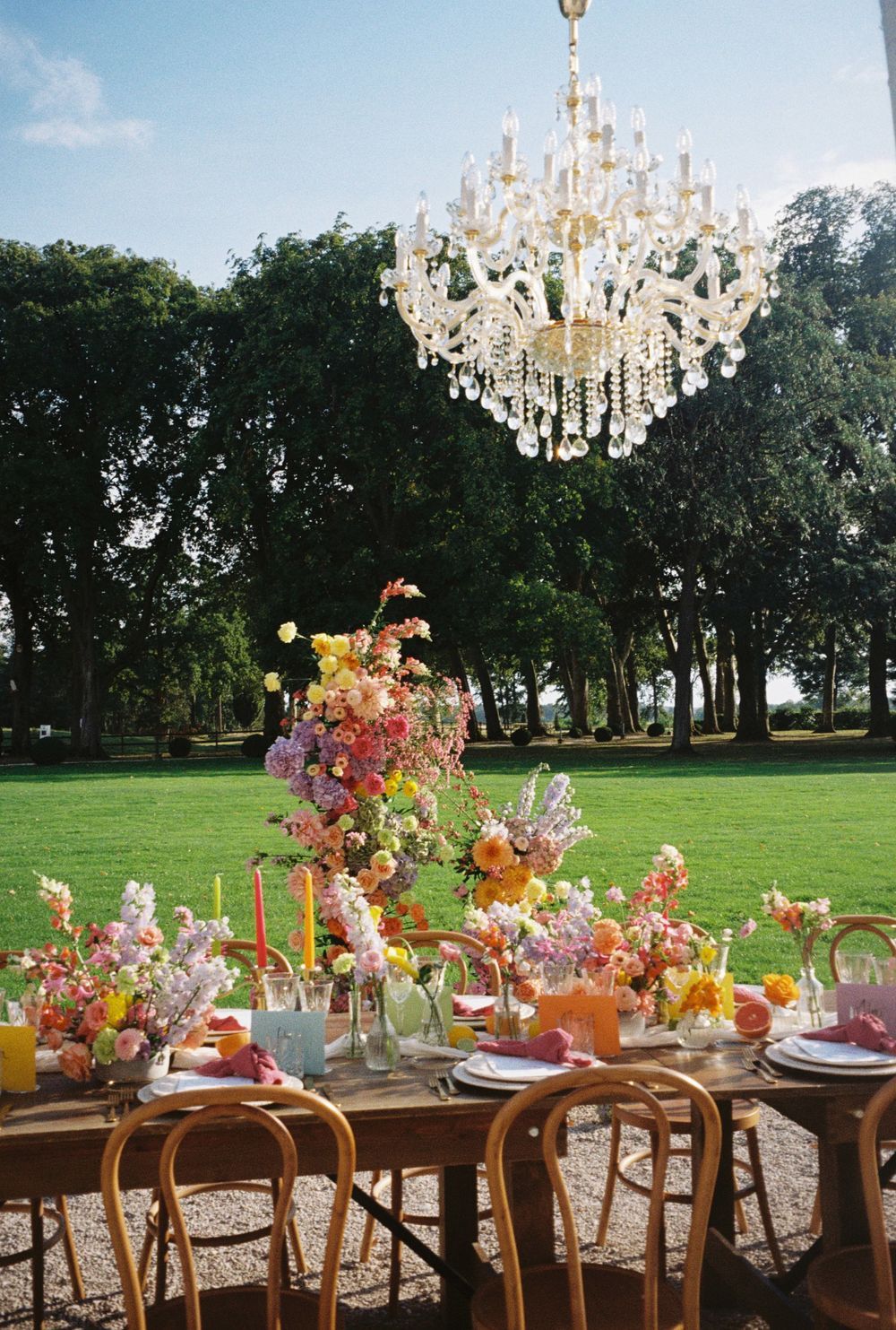 Elegant outdoor wedding reception table with crystal chandelier and colorful autumn floral arrangements.