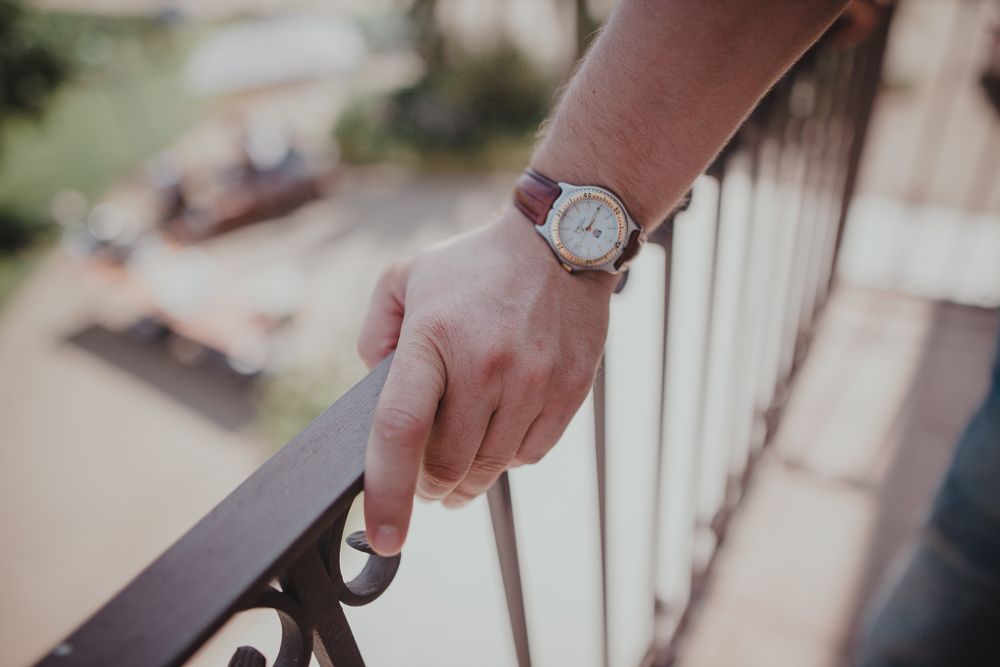 Close-up of a wristwatch against a railing in soft focus.