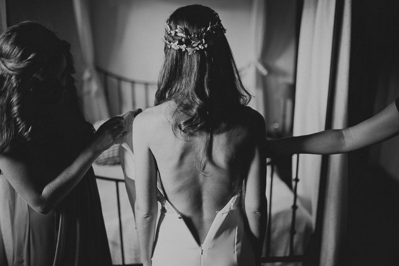 Black and white photo showing the back of an elegant backless wedding dress with delicate hair accessories.