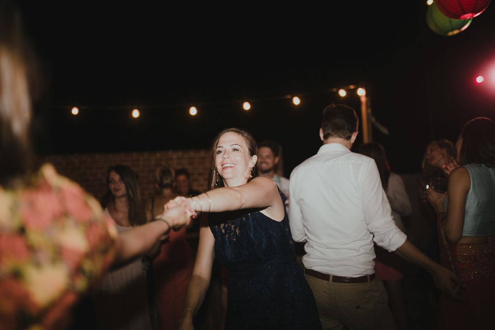People dancing together at outdoor evening party under ambient string lighting.