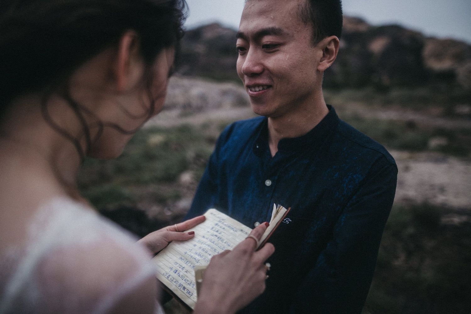 A couple exchanges written vows or notes while standing in a dramatic rocky landscape.