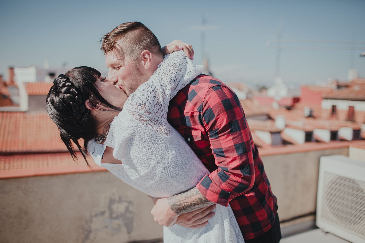 A romantic dip pose between a couple on a rooftop with Spanish architecture in the background.