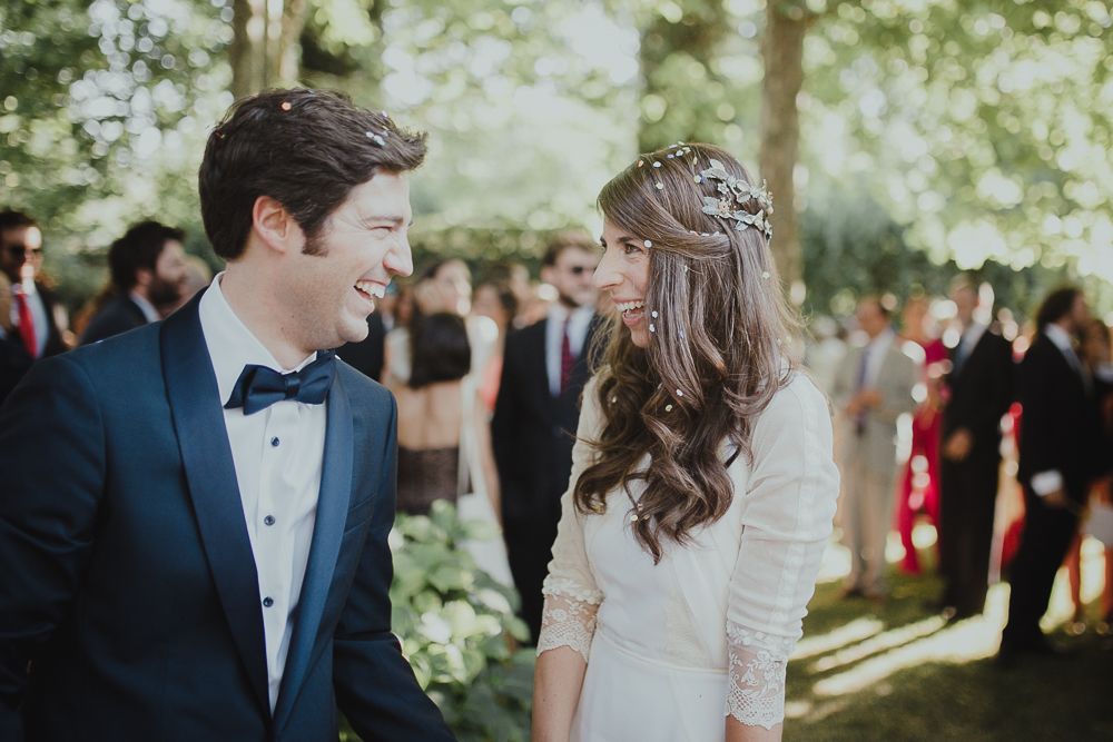 Couple shares joyful moment during outdoor garden wedding with guests in background.