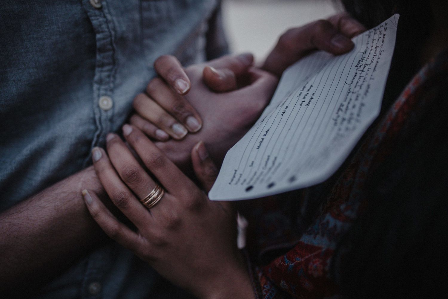 Close-up shot of hands holding a document with rings visible in warm lighting.
