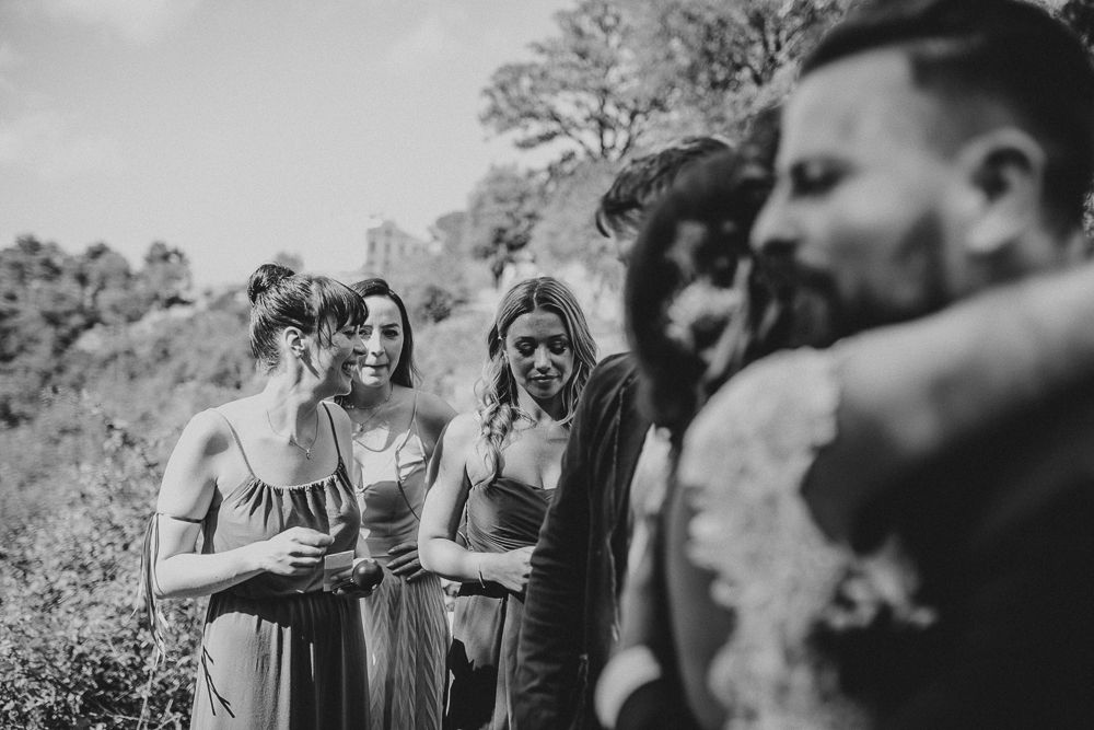 Wedding guests gathered outdoors in formal attire watching a ceremony.