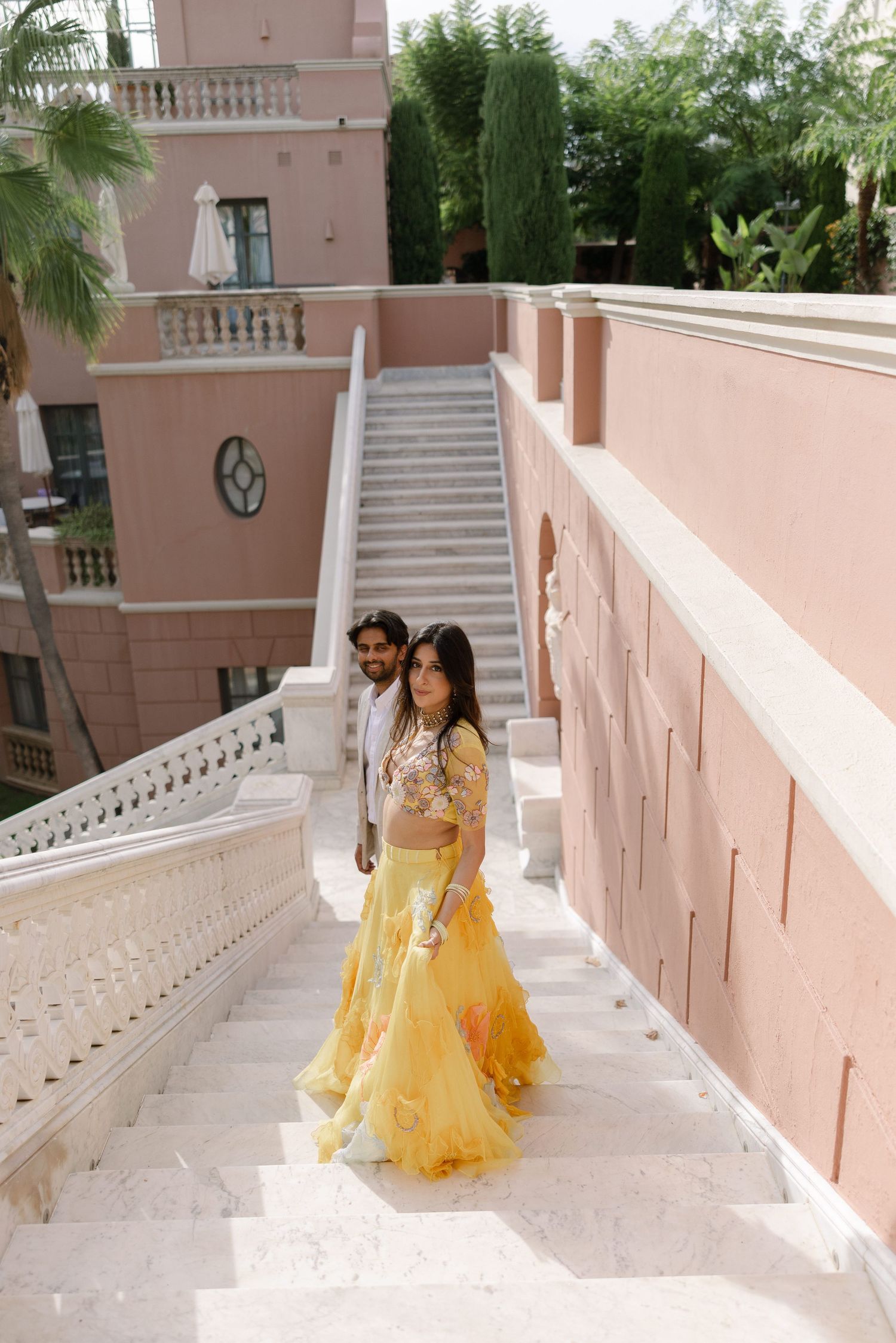Elina and Jag walking along the marble staircase between pink walls.