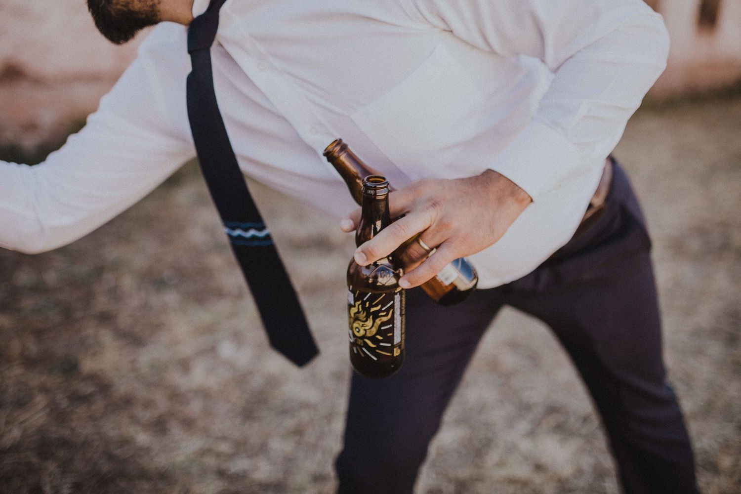 Person in formal attire holding beer bottle against desert backdrop.
