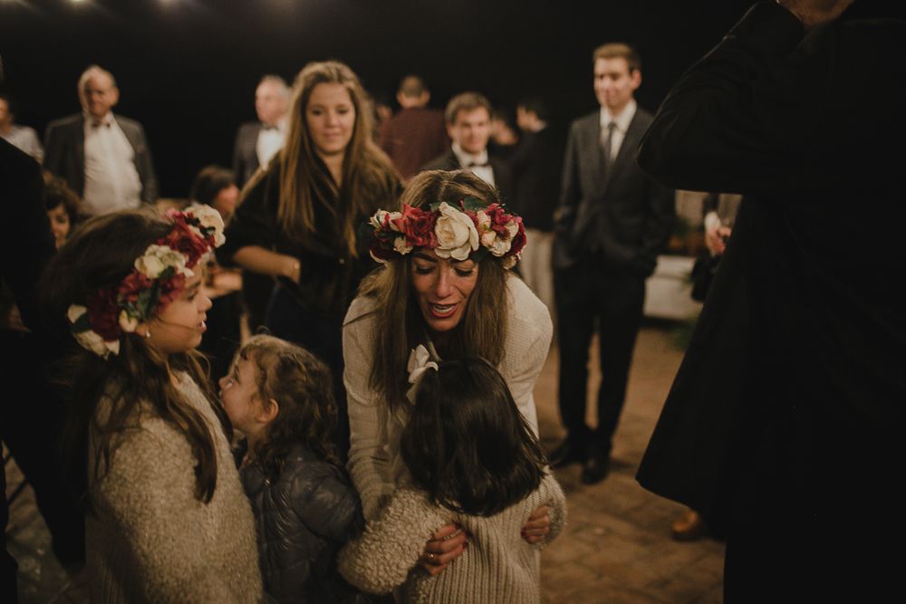 Party guests wearing floral crowns celebrate at an indoor event.