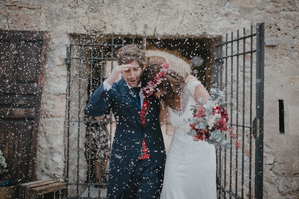 Newlyweds share a joyful moment under falling confetti outside a stone building.