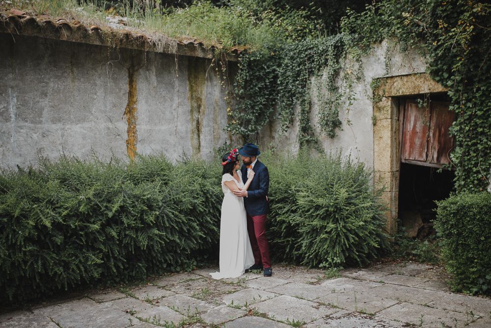 Wedding portrait in garden courtyard with rustic stone walls and overgrown foliage.