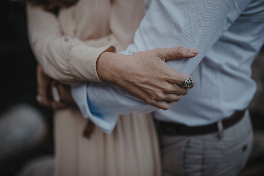 Close-up detail shot of hands embracing, showcasing casual formal wear against a natural backdrop.