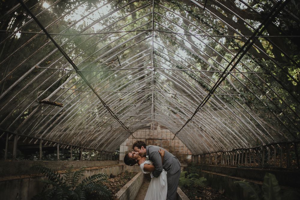 Wedding couple embracing inside an old greenhouse with dramatic natural lighting.