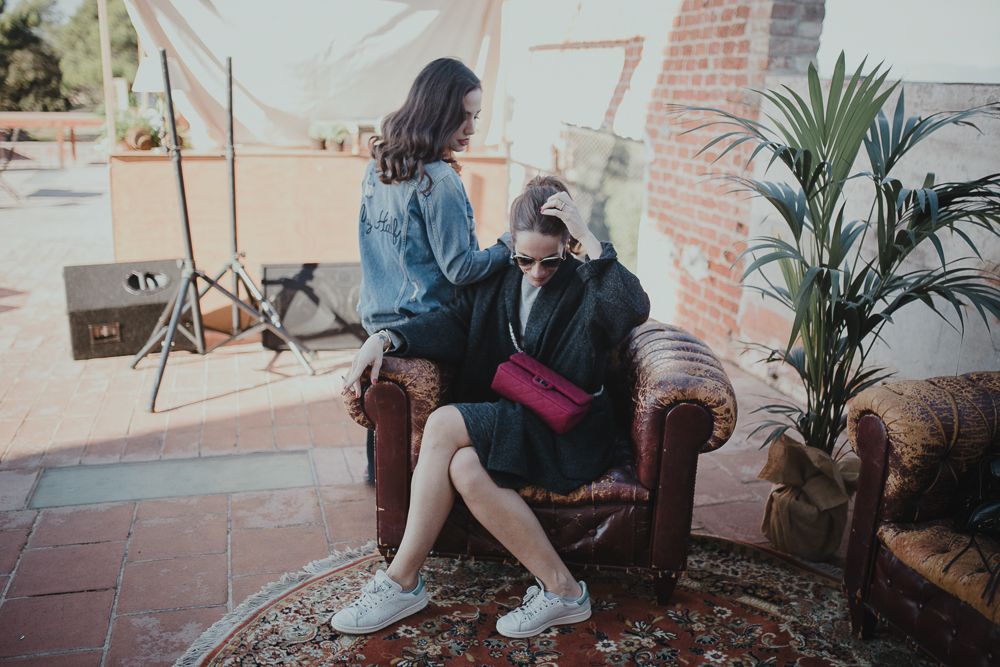 Two people relax on a vintage couch surrounded by indoor plants and decor.