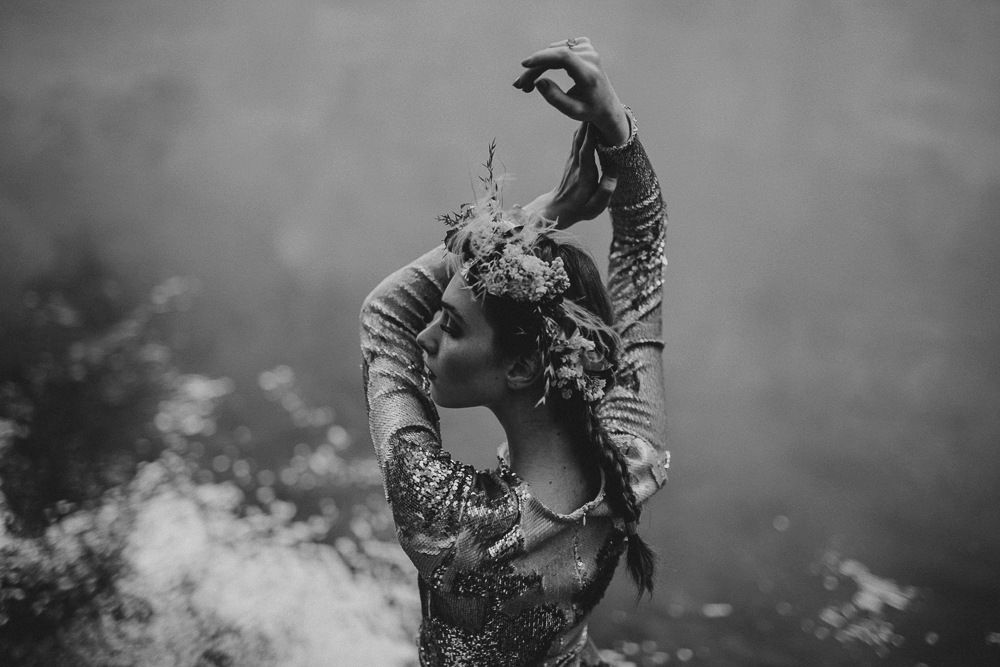 Artistic black and white portrait of figure wearing floral crown with dramatic sky.